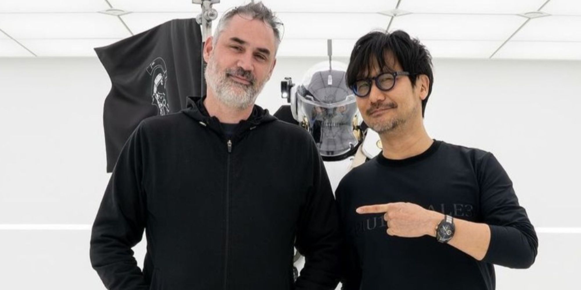 Hideo Kojima pointing to director Alex Garland in a picture by the Kojima Productions Ludens Mascot.