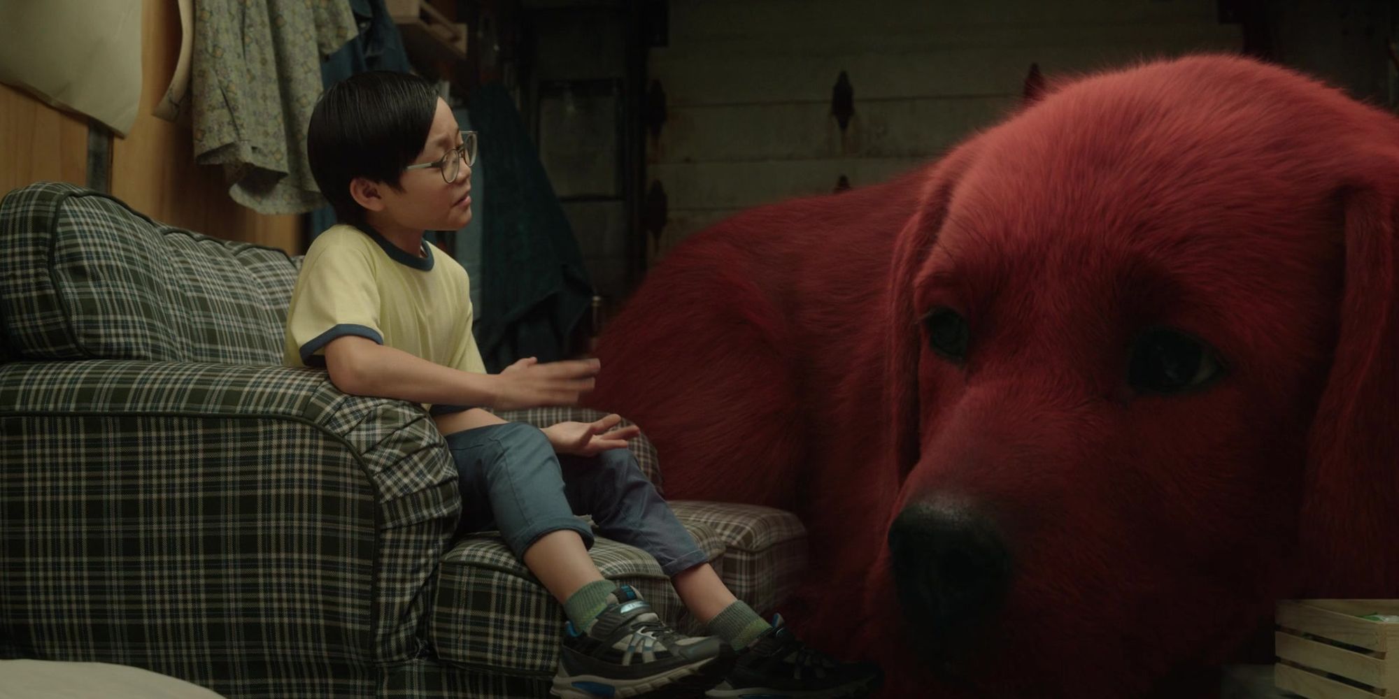 A child talks to a massive red dog while sitting in a chair.