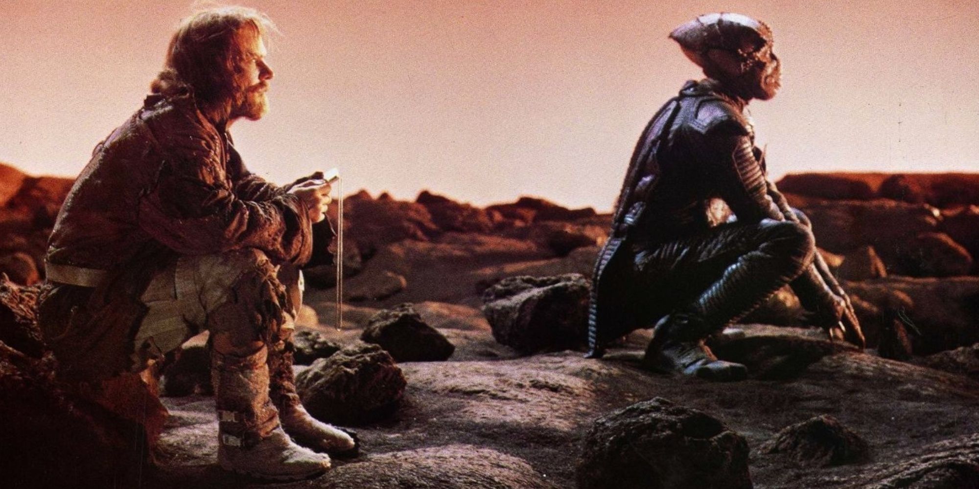A human and an alien soldier, former enemies, sit together on a barren planet.
