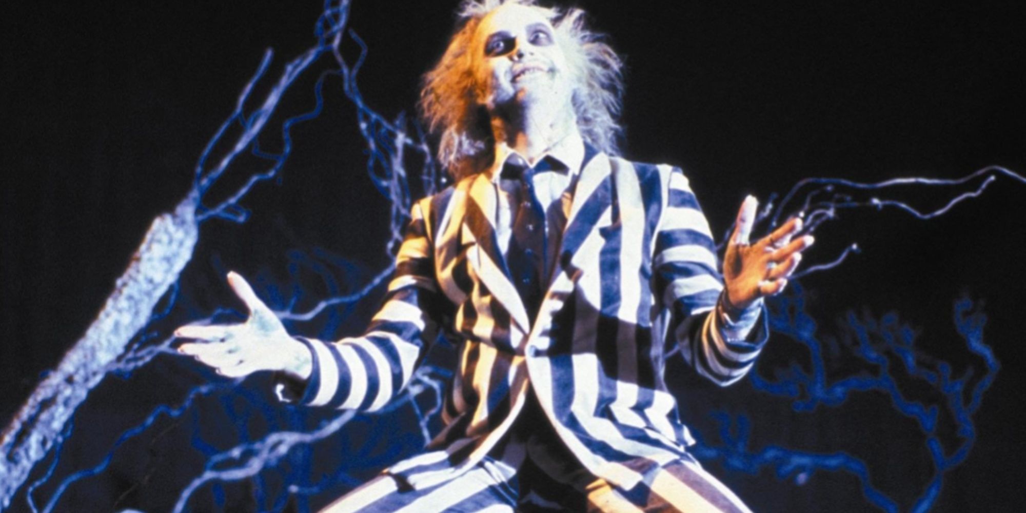 Michael Keaton's character Betelguese in the black and white striped suit on his knees with arms raised as though he's presenting something.