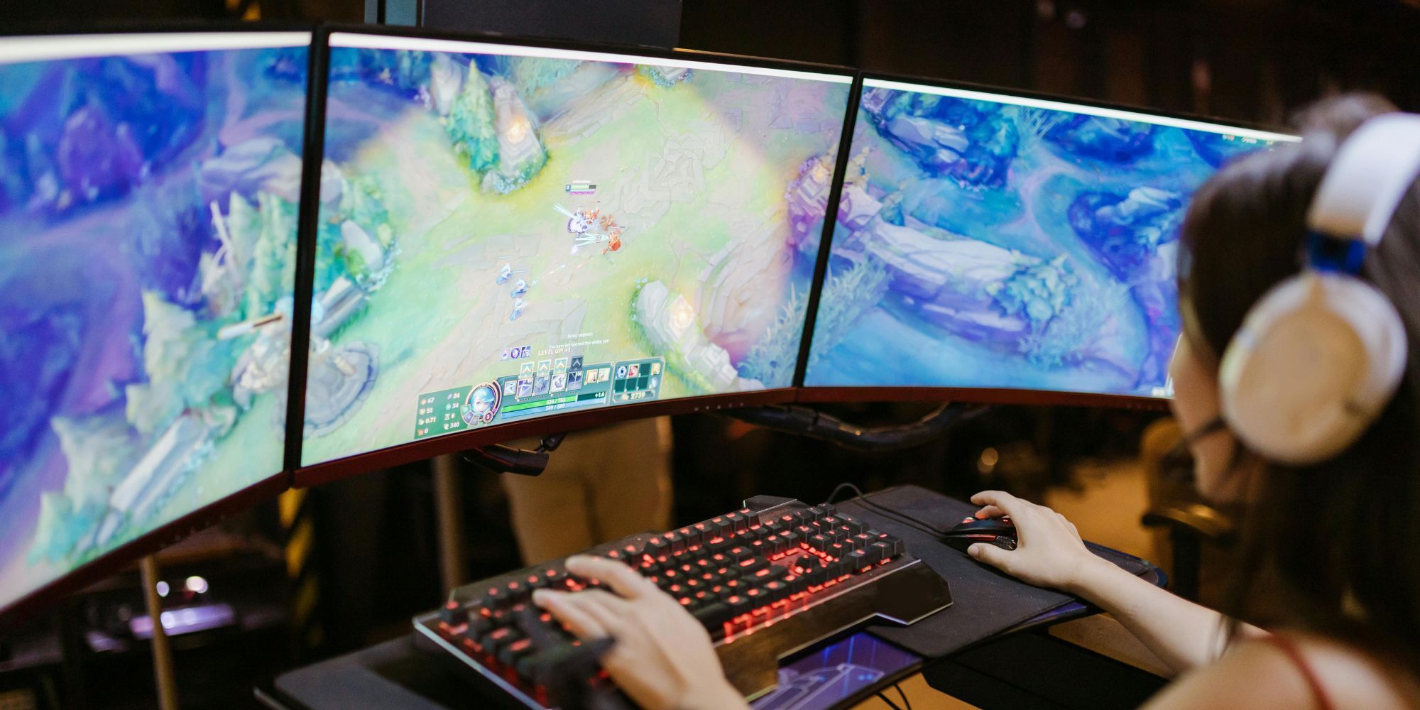 Person Playing League Of Legends On Triple Monitor Set Up With Red RGB Keyboard