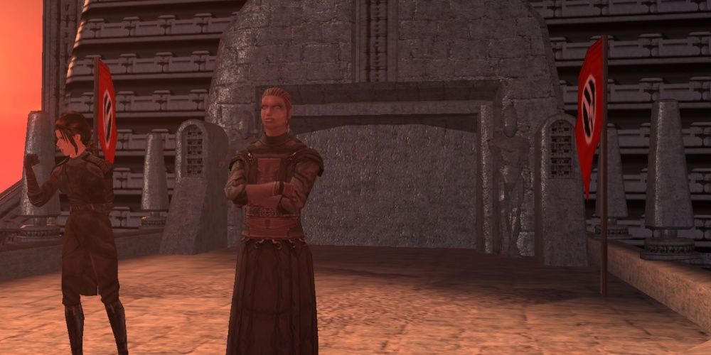 Two characters stand in front of stone building with flags nearby