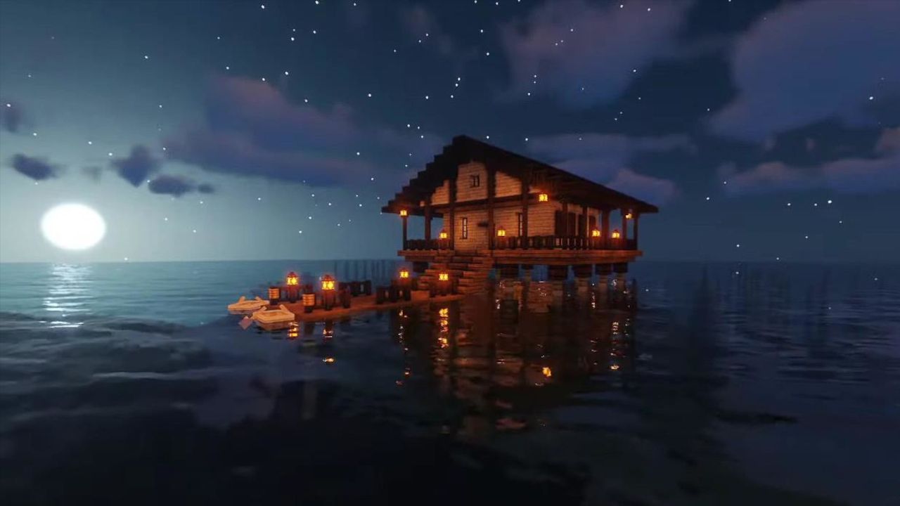 A Minecraft beach house on stilts in the water, with a dock stretching out front, all lit by lanterns at night.