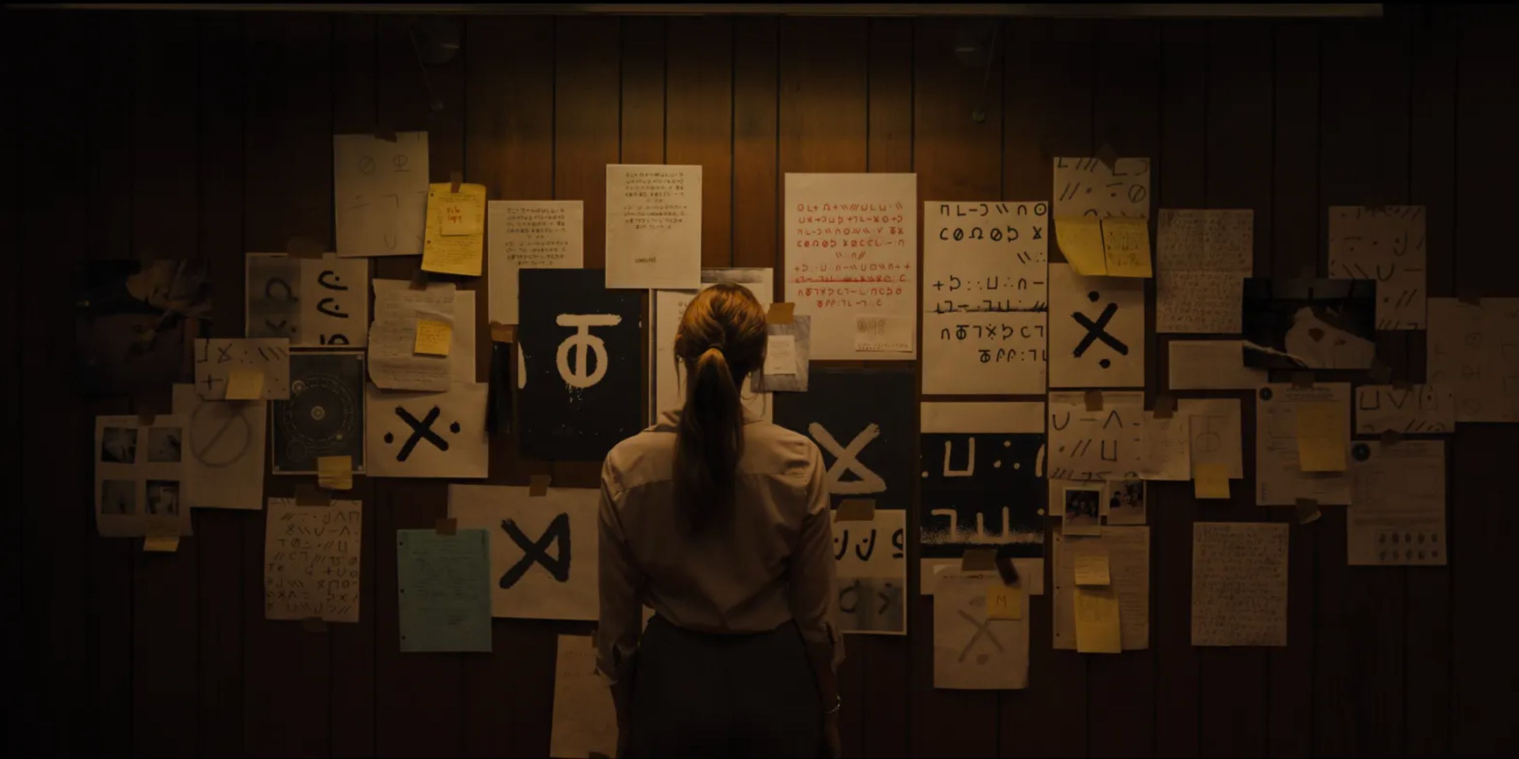 Screenshot from Longlegs movie trailer featuring a woman studying a wall full of clues