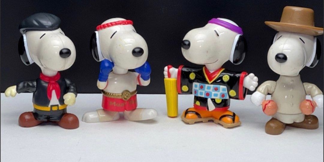 Four Snoopy toys, each one in a different national costume, stand against a black background.