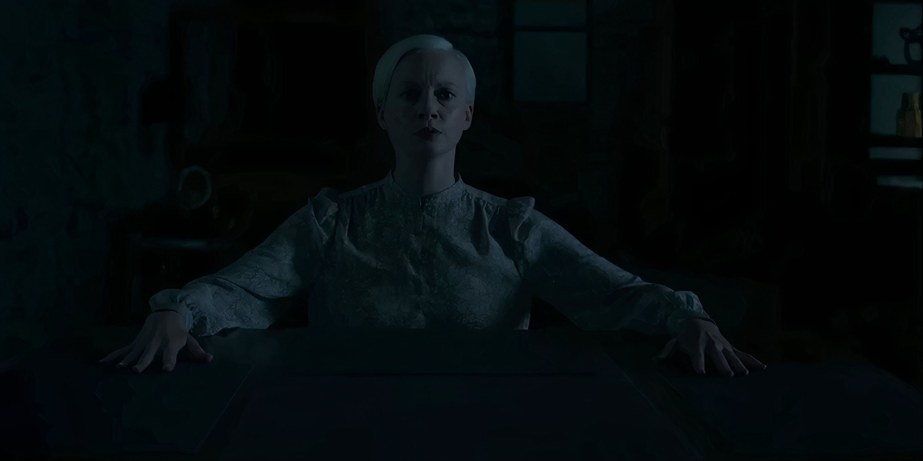Darci sits in the dark with her hands on the table in Oddity.