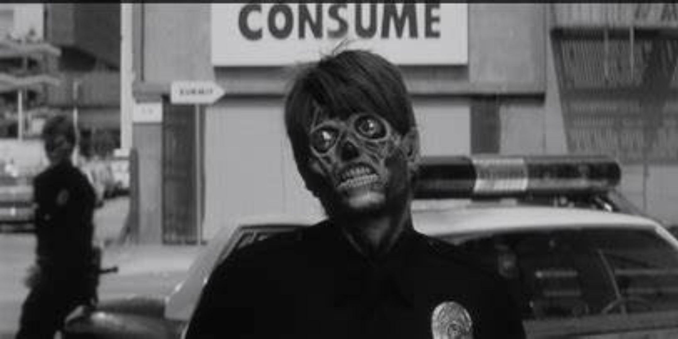 An alien disguised as a police officer in front of a propaganda screen in They Live.