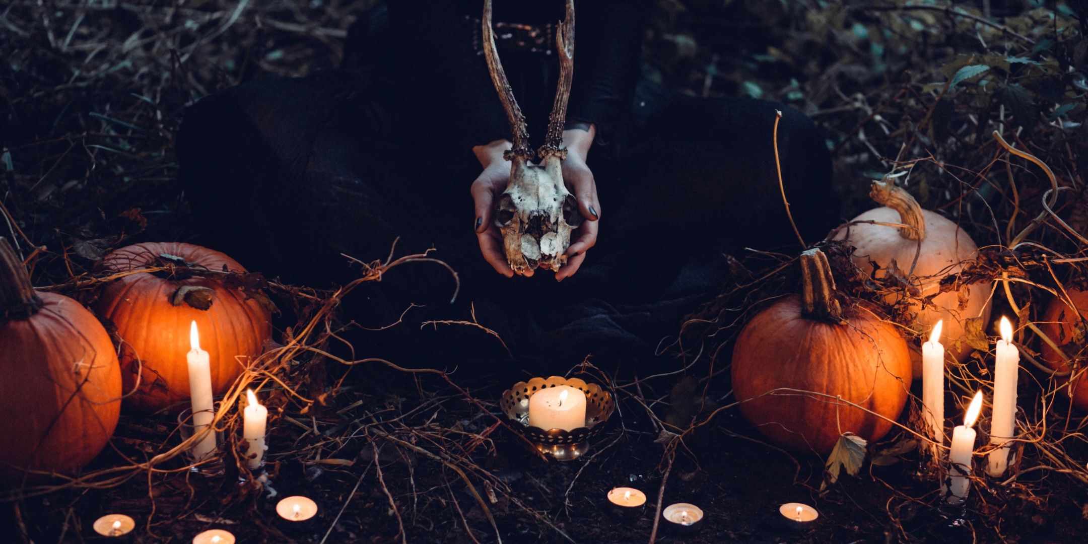A witch holding a skull and surrounded by pumpkins.