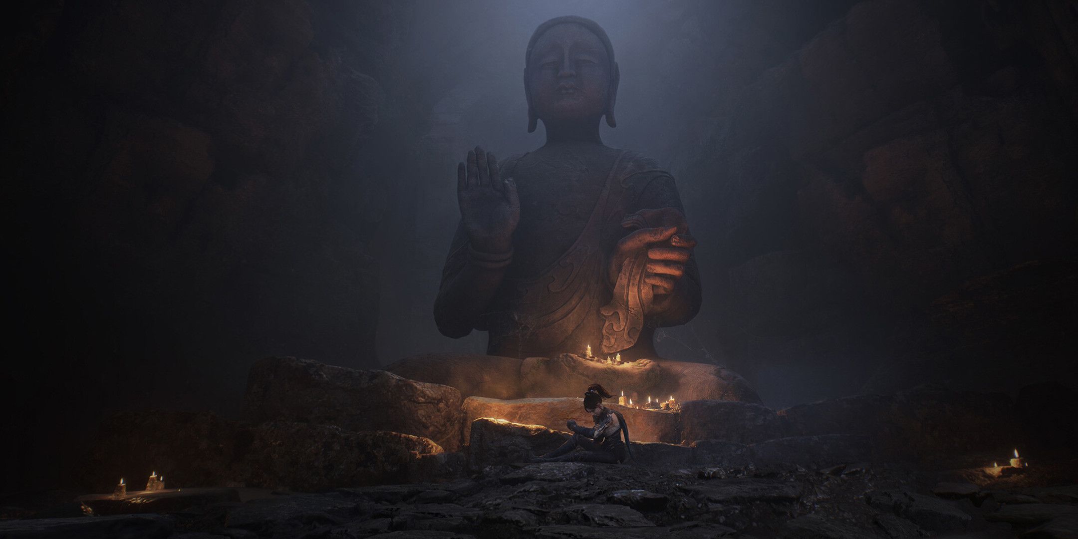 A woman sat underneath a large Buddha statue.