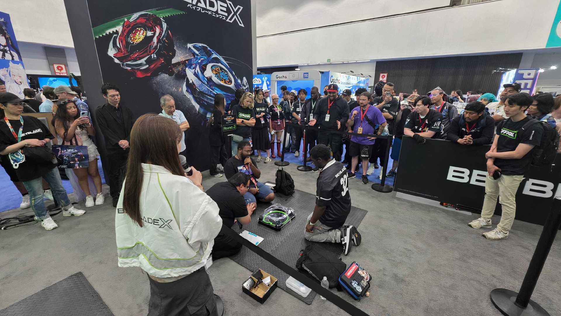Beyblade X Tournament Players On The Floor While MC Comentates.