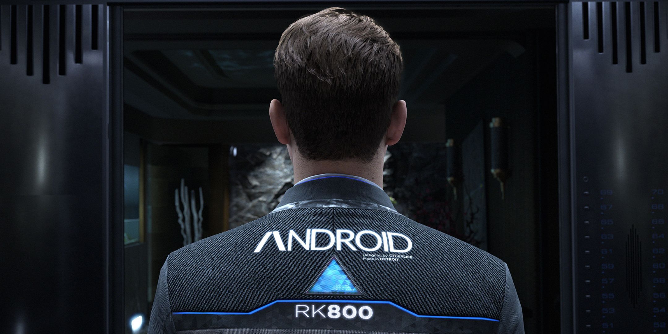 The back of a man's head. The man appears to be a human-looking android, and his clothing labels him as such.