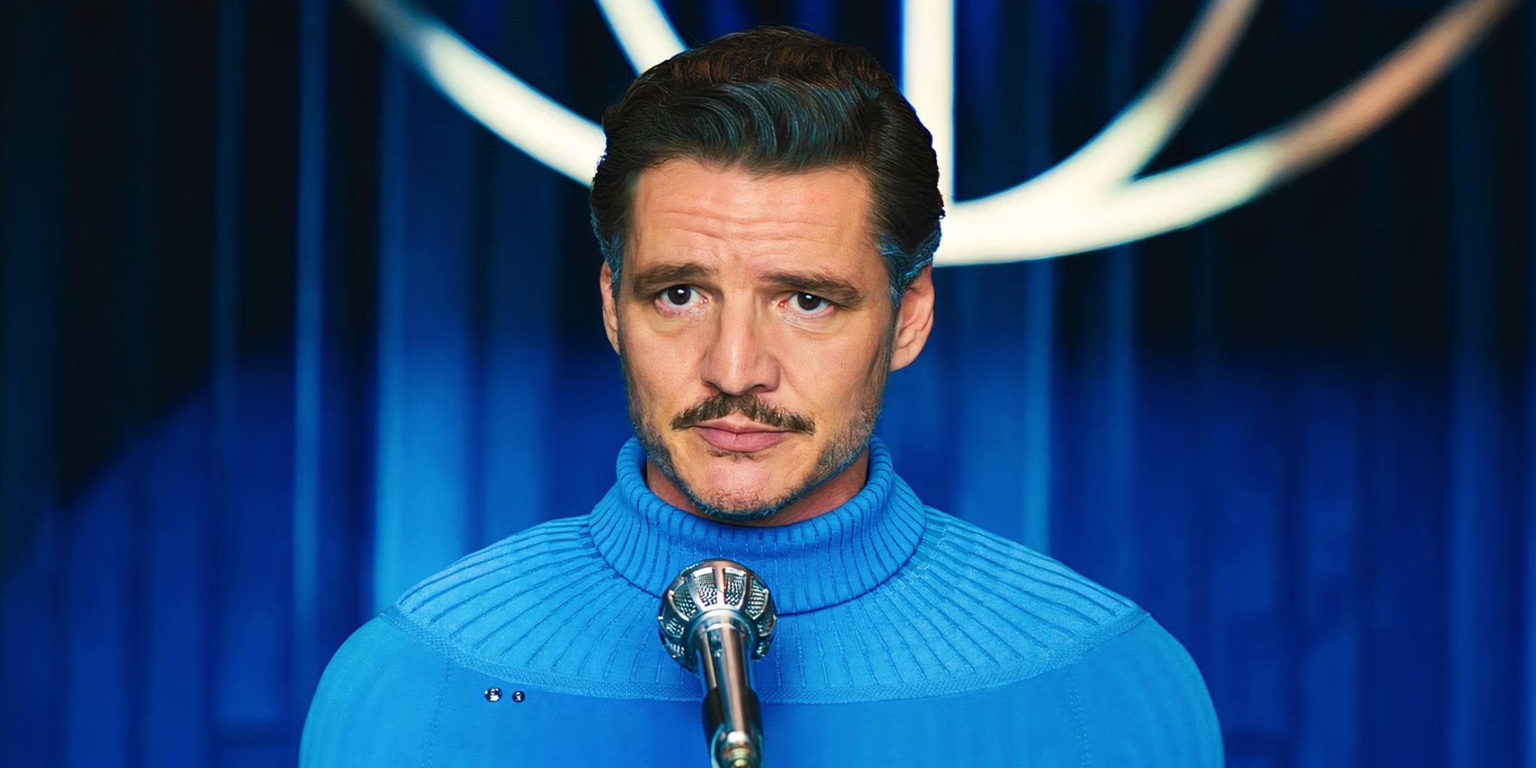 Pedro Pascal as Reed Richards in Fantastic Four: First Steps. He is wearing a blue turtleneck and stands in front of a microphone.