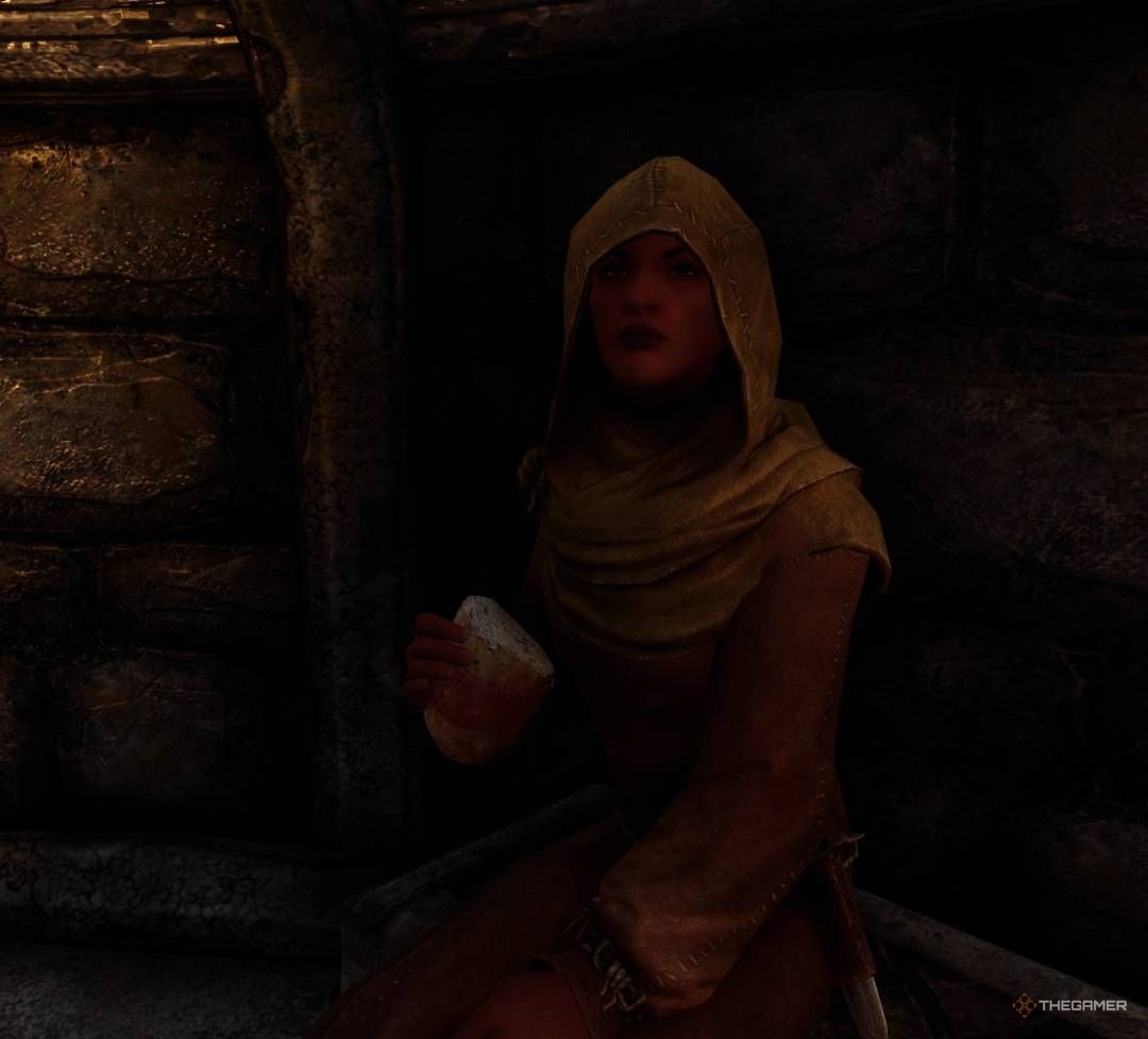 Anwen sits while eating a piece of bread inside deep dark Temple of Dibella Inner Sanctum in Skyrim.