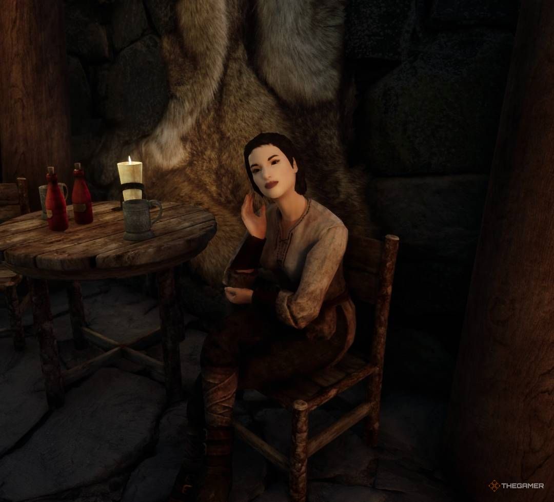 Sylgja sits in chair and rests her head against her hand inside her home in Shor's Stone, Skyrim.