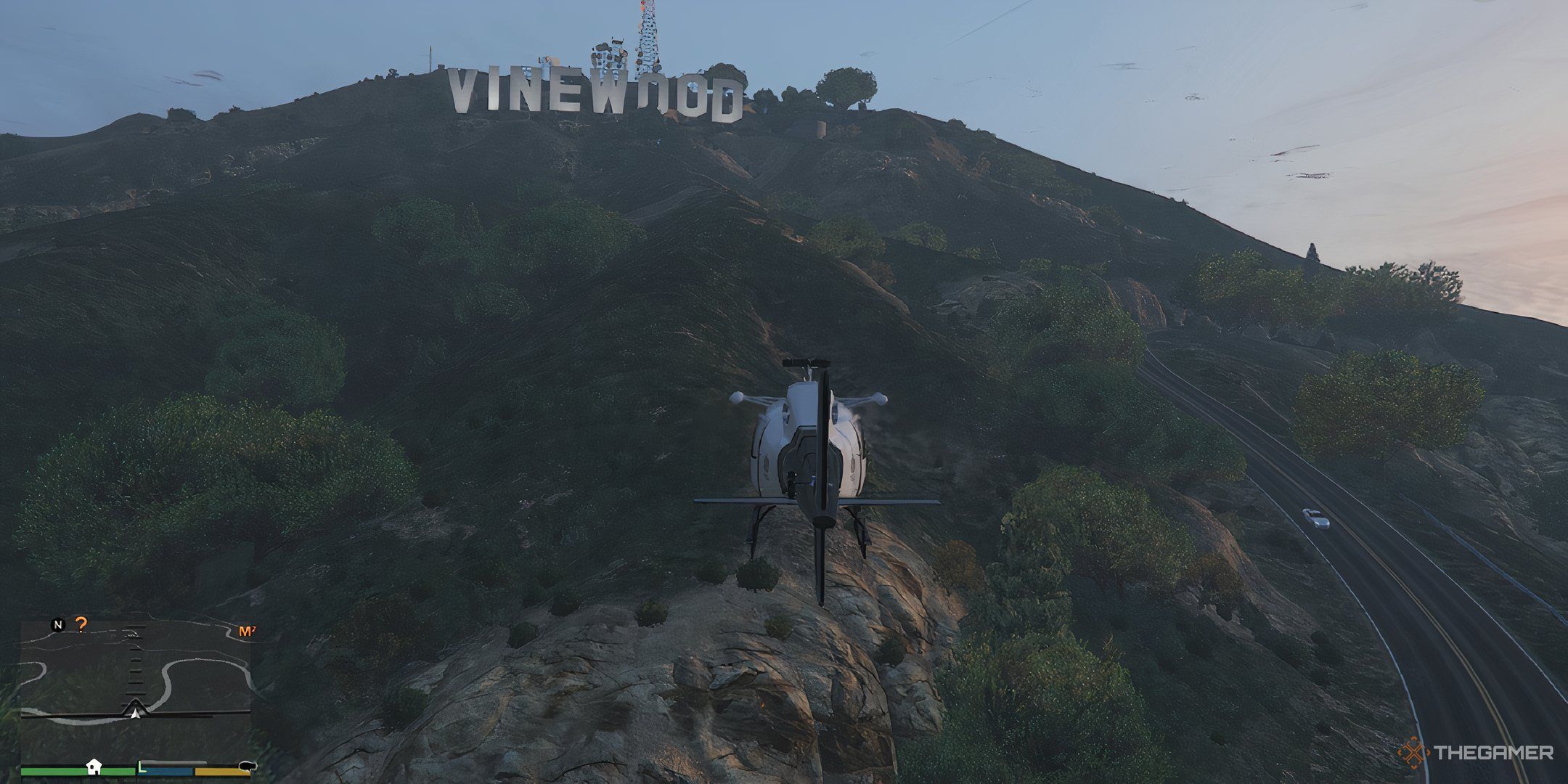 A gameplay screenshot of Grand Theft Auto 5, showing a helicopter idling in front of the Vinewood sign in Los Santos.