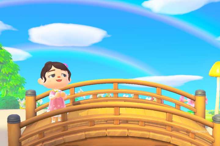Animal Crossing player standing on a bridge with a double rainbow in the background.