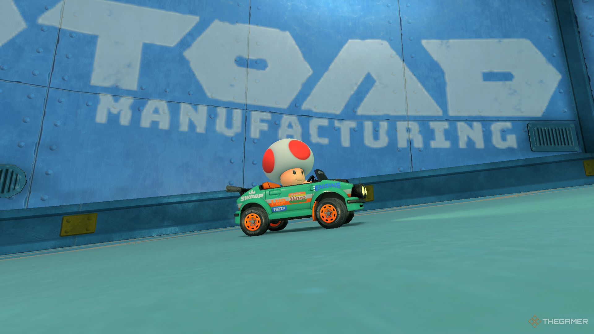 Toad driving past the words Toad Manufacturing painted on a steel wall in Mario Kart World