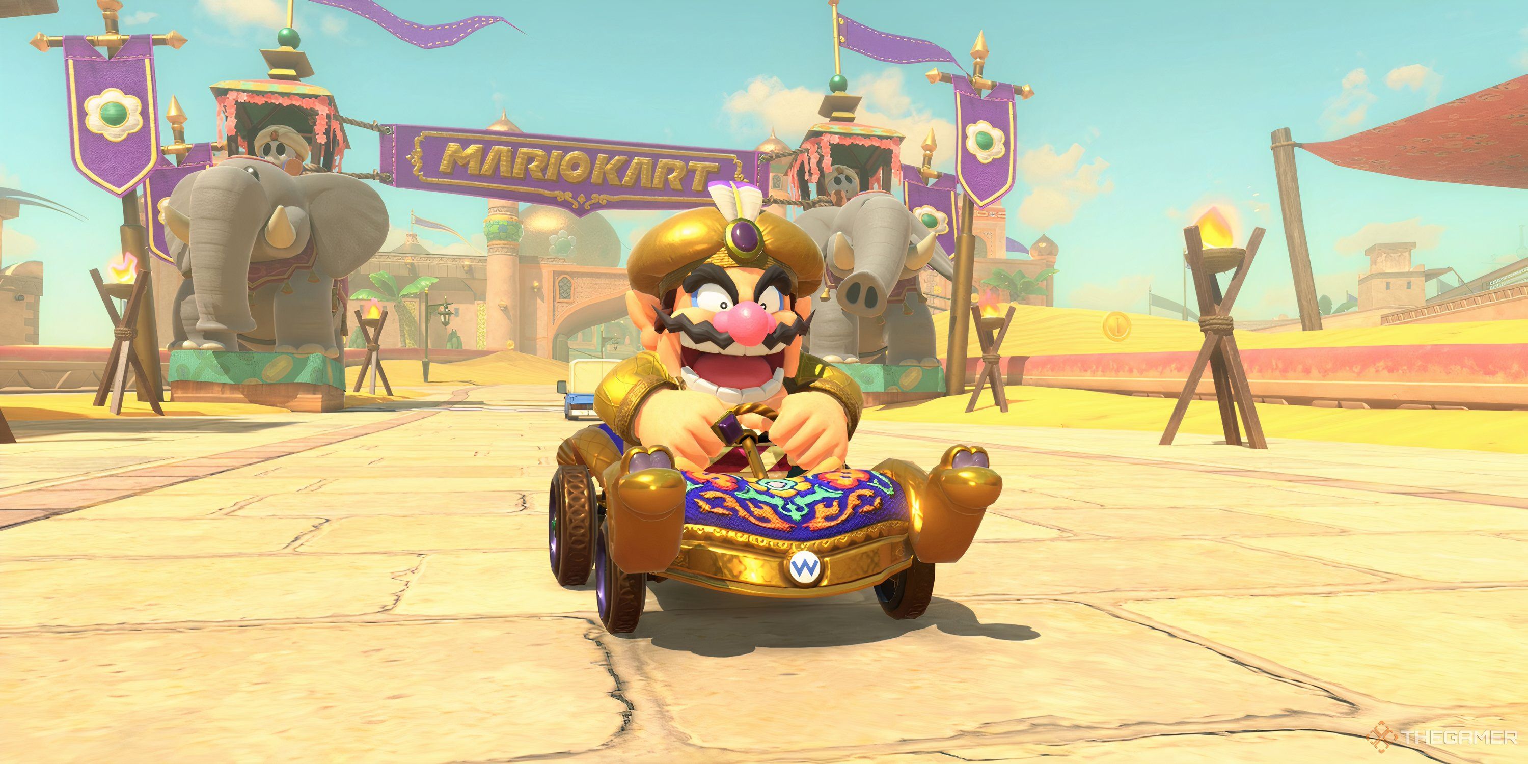 Wario drives the Carpet Flyer outside Shy Guy Bazaar while wearing the Oasis outfit in Mario Kart World.