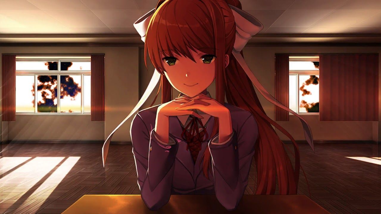 Monika sitting at a table with hands under her chin, looking at the camera