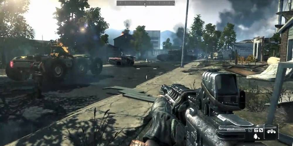 Gun aiming at a battered car with buildings and smoke in the background.