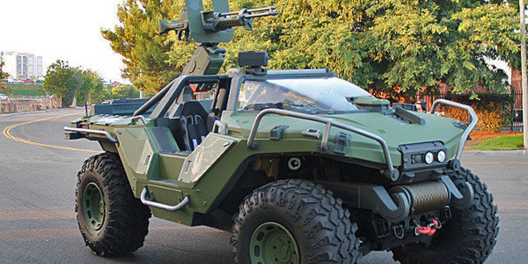 Best Vehicles a real life Warthog from Halo sat still on a road with trees and a city in the background