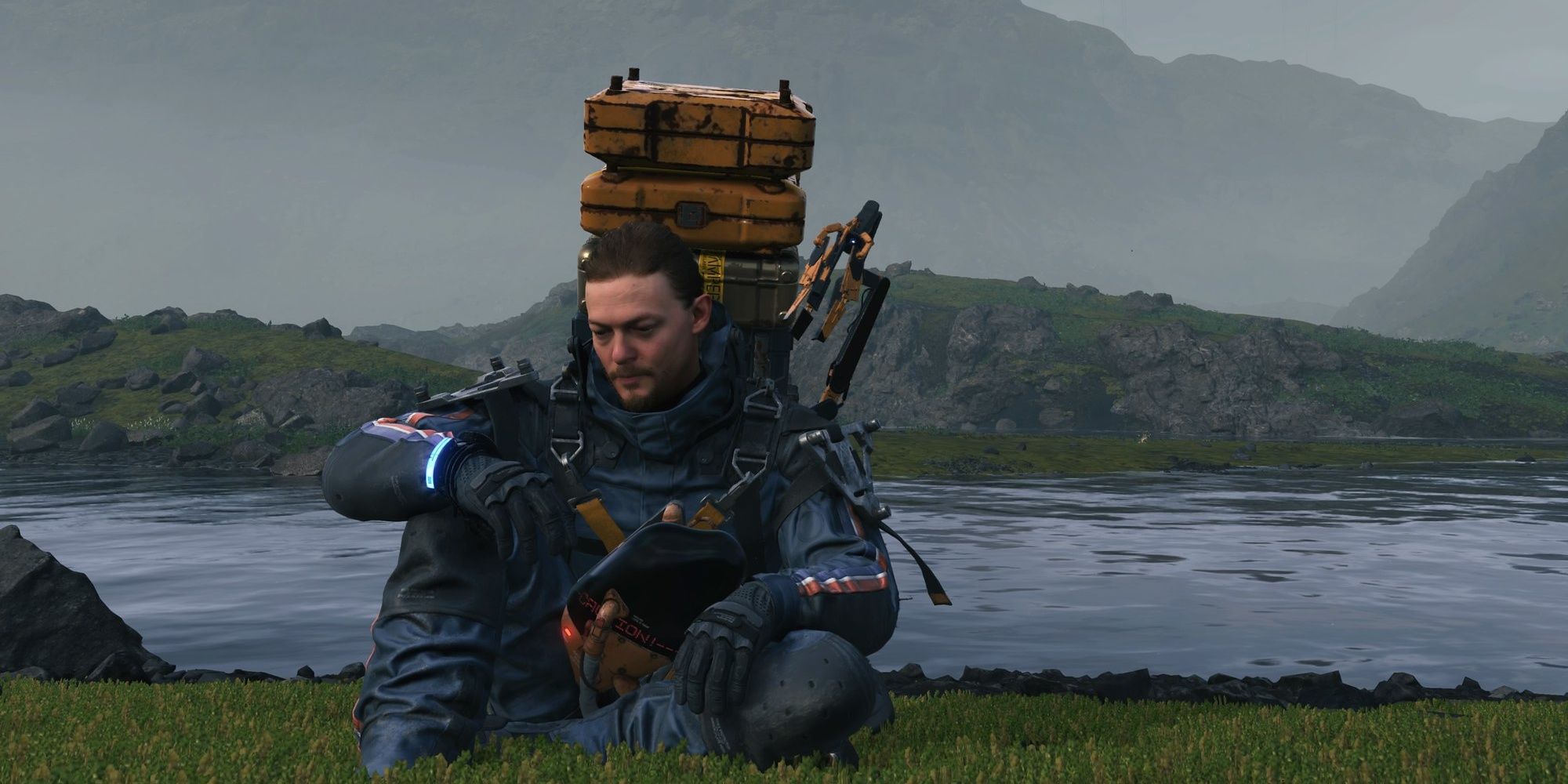 Death Stranding Sam Resting with cargo on his back and a river and misty mountains in the background