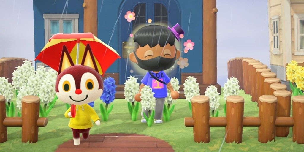 An Animal Crossing player using the Joy reaction in front of a villager's blue house. Beside them, Rudy walks around with an umbrella