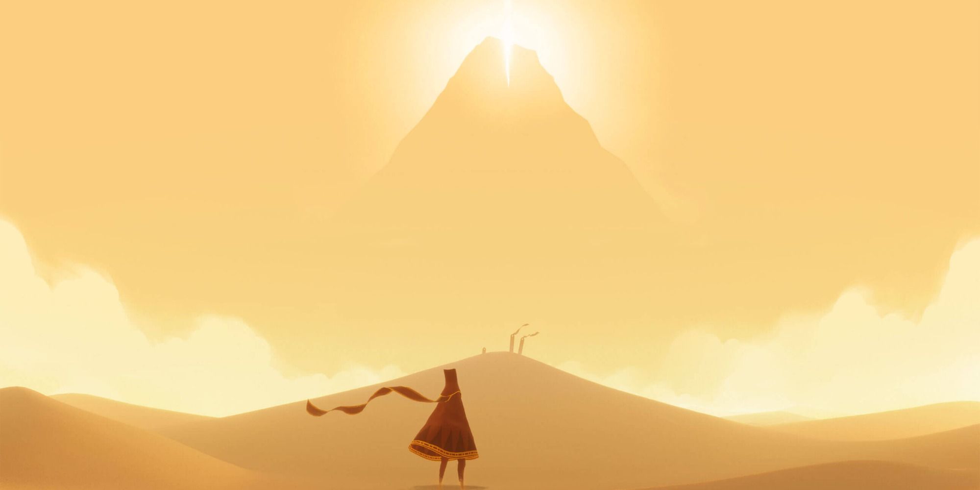 The main character of Journey stands in a desert at the base of a mountain, looking up at a glowing light at the top of the peak