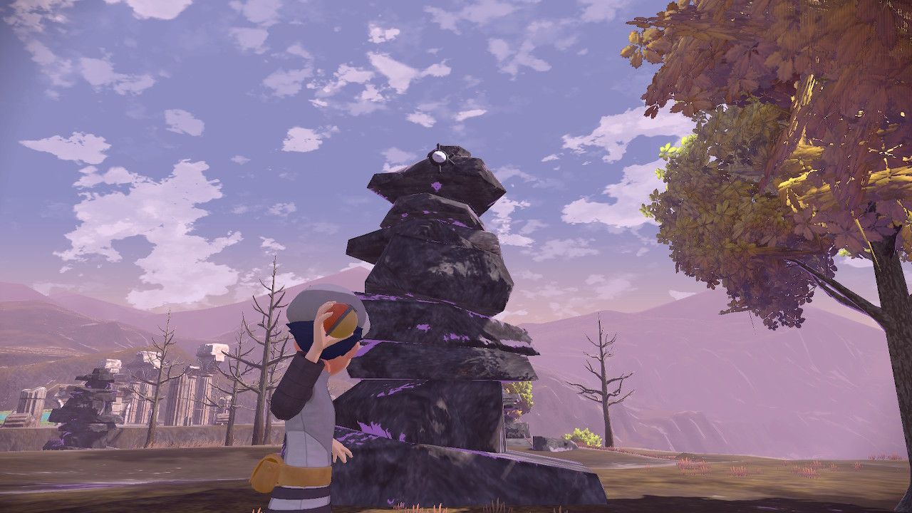 Pokemon Trainer aiming his pokeball at Unown K, who sits on top of a stone monument in Pokemon Legends Arceus.
