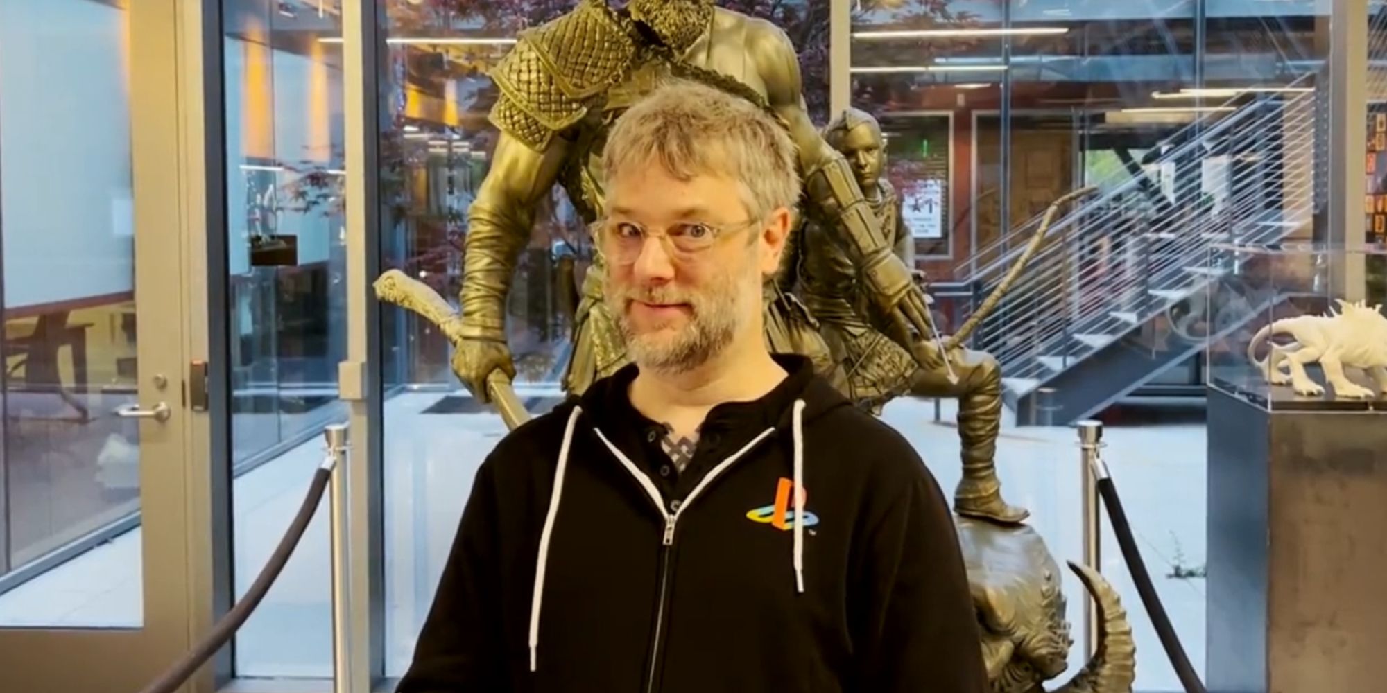 Cory Barlog stood in front of a statue of Kratos and Atreus
