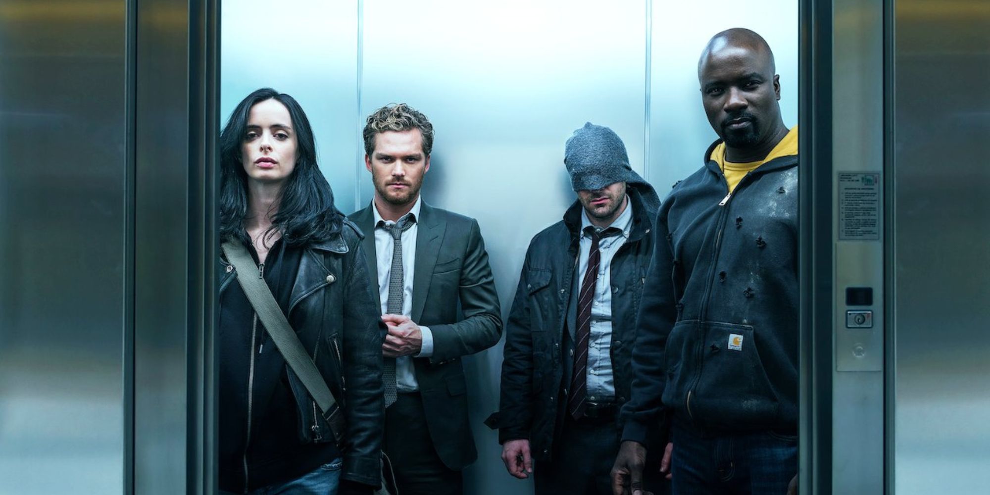 a wide angle shot of The Defenders stood in an elevator with Jessica Jones on the left, Iron Fist next to her, Daredevil to his right and Luke Cage on the far right