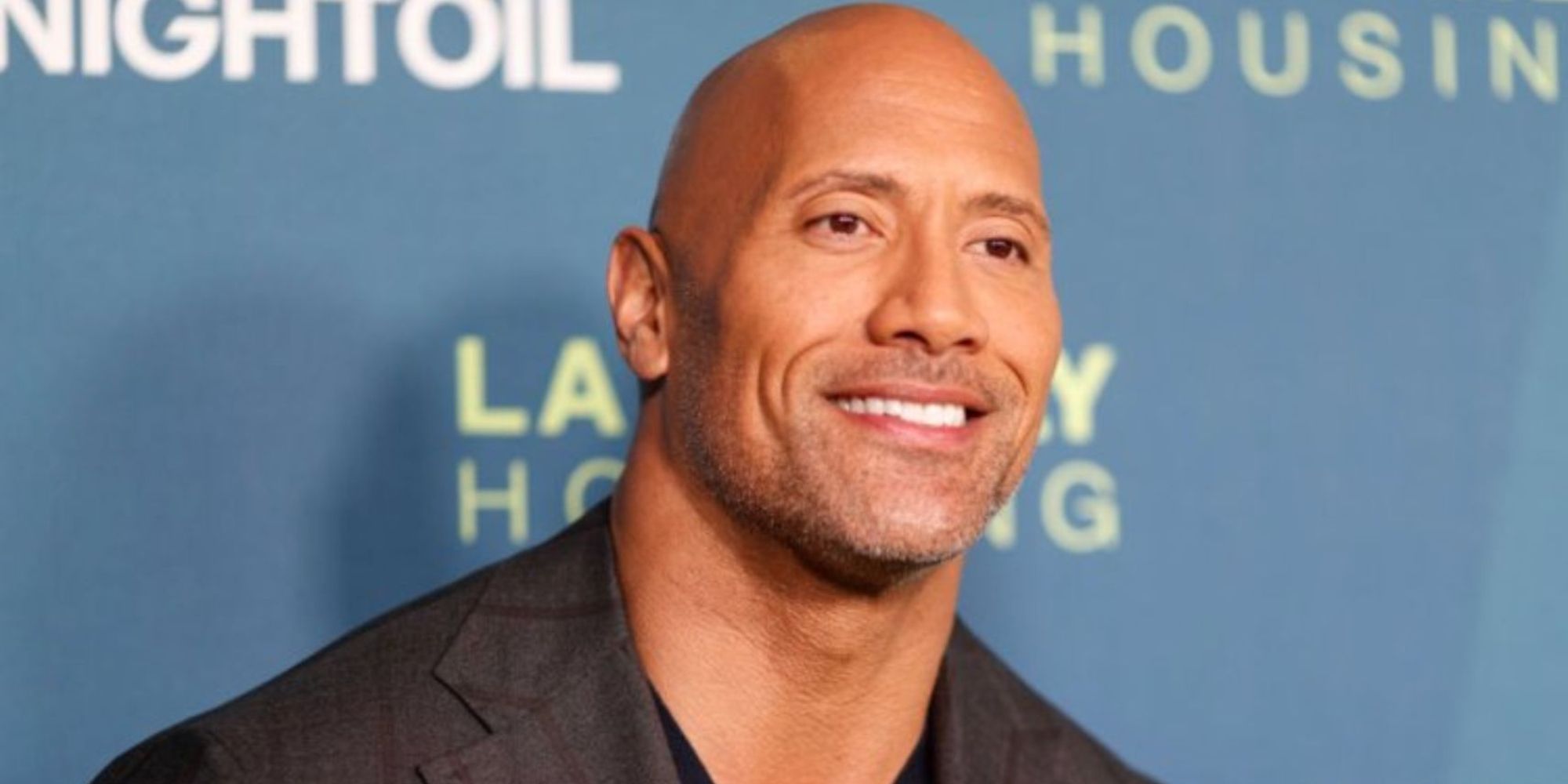 a photograph of Dwayne "The Rock" Johnson smiling at a camera off picture while at an event 