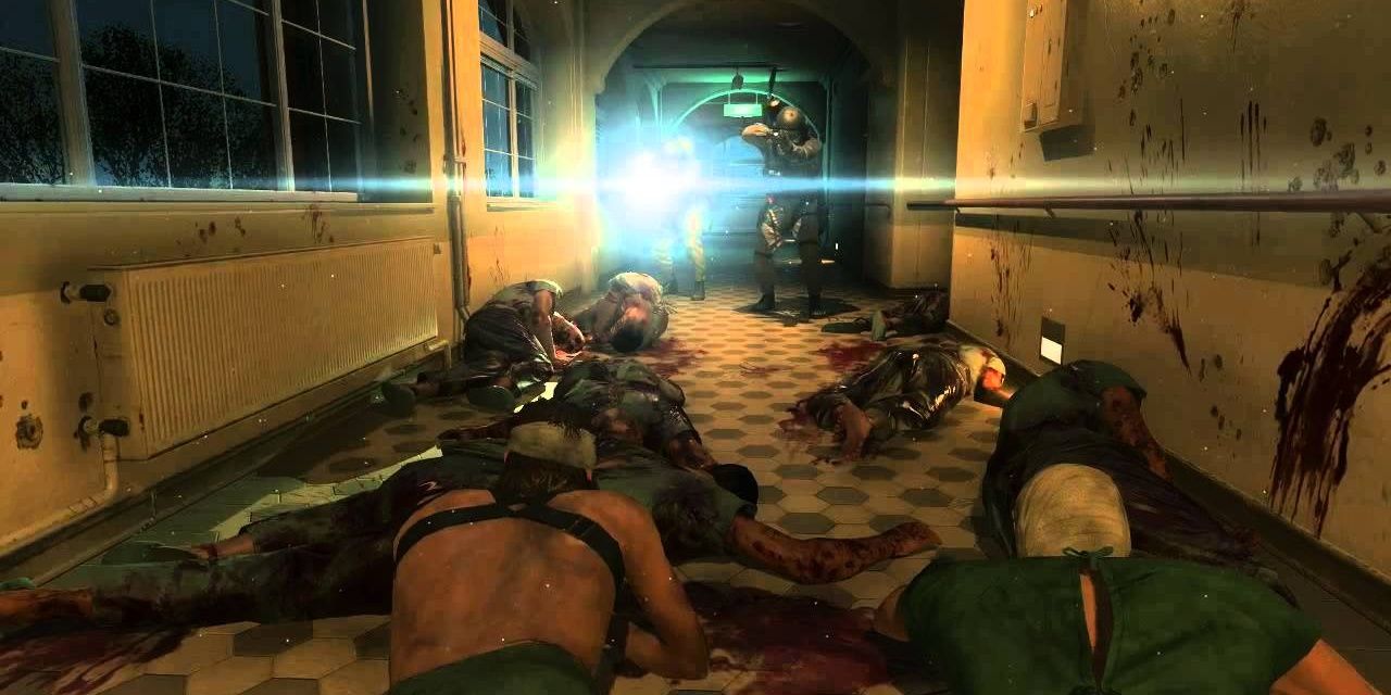 Snake and Ishmael prone in a corridor amongst bodies with soldiers with a flashlight in front of them 
