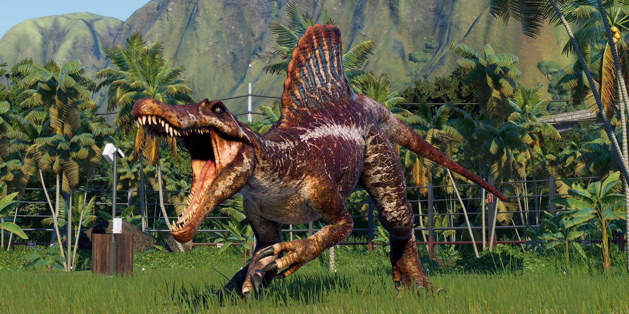 a mid shot of a dinosaur from Jurassic World Evolution 2 with its mouth wide open roaring with tropical trees and a mountain in the background