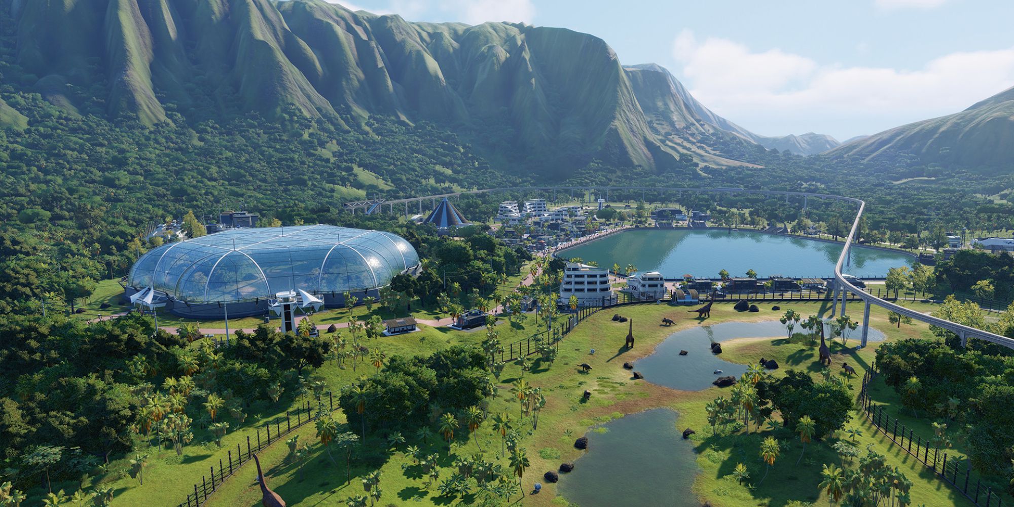 a wide shot of a lush and verdant park in Jurassic World Evolution 2 surrounded by trees, water and mountains