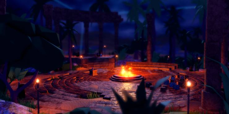 A firepit blazes in the middle of a stone courtyard with benches on the opposite side of it