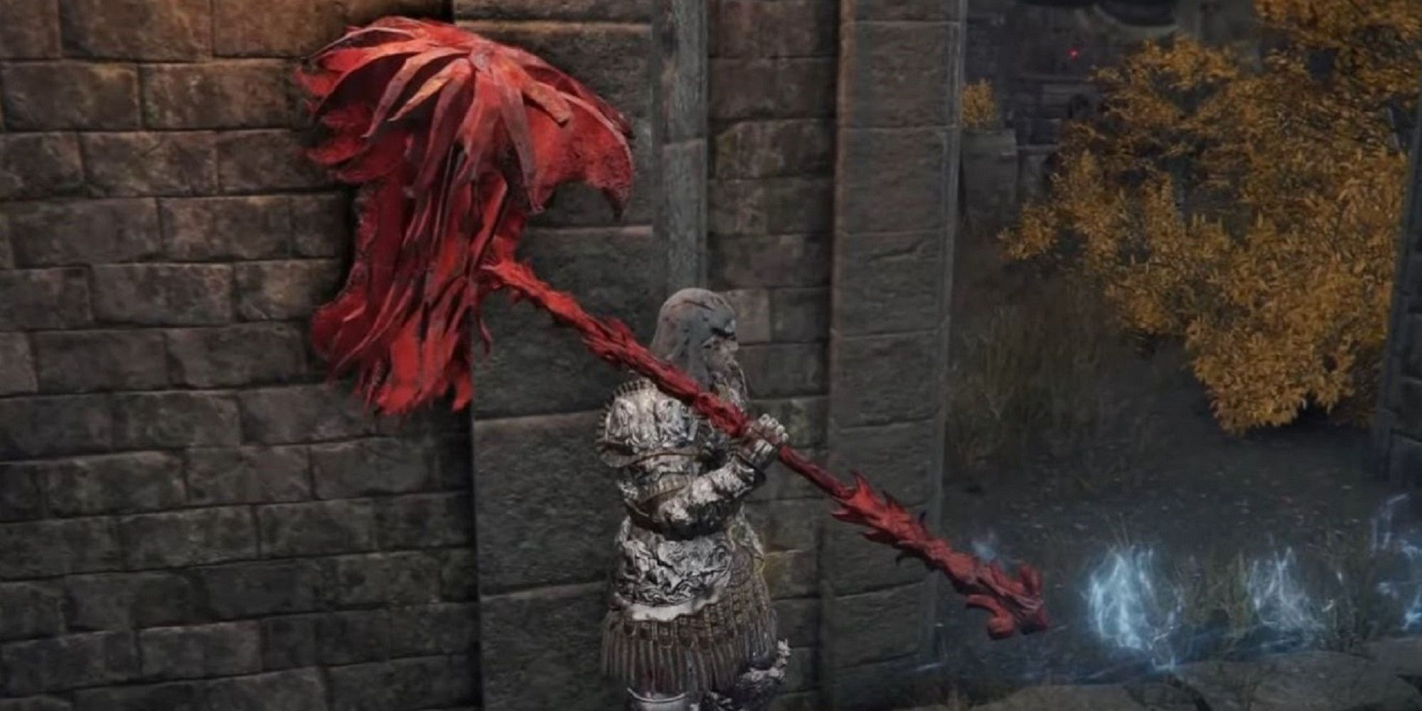 Elden Ring character holding the bright red Prelate's Inferno Crozier weapon and standing by a wall