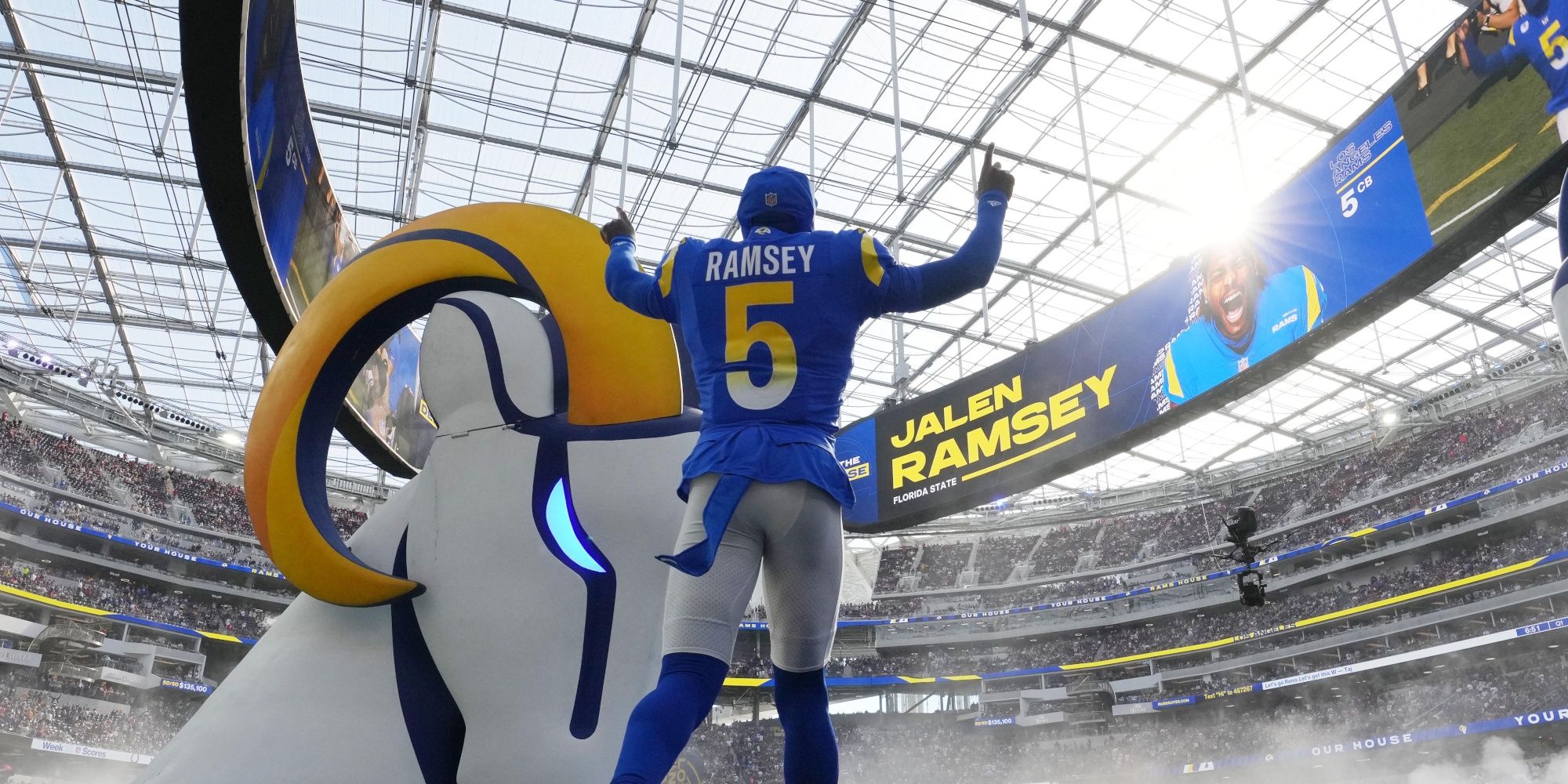 Jalen Ramsey making his entrance at a Rams game in a blue uniform. His name is displayed above him on a giant stadium wrap around video wall
