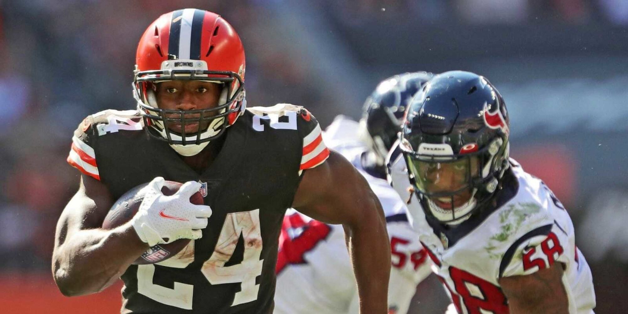 Nick Chubb breaking away from defenders in brown Browns jersey