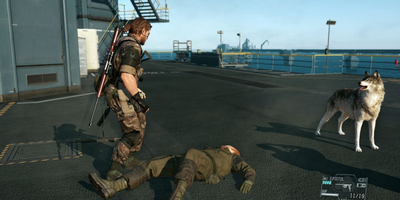 Venom Snake stands over one of his unconscious employees at Motherbase, with D-Dog at his side. 