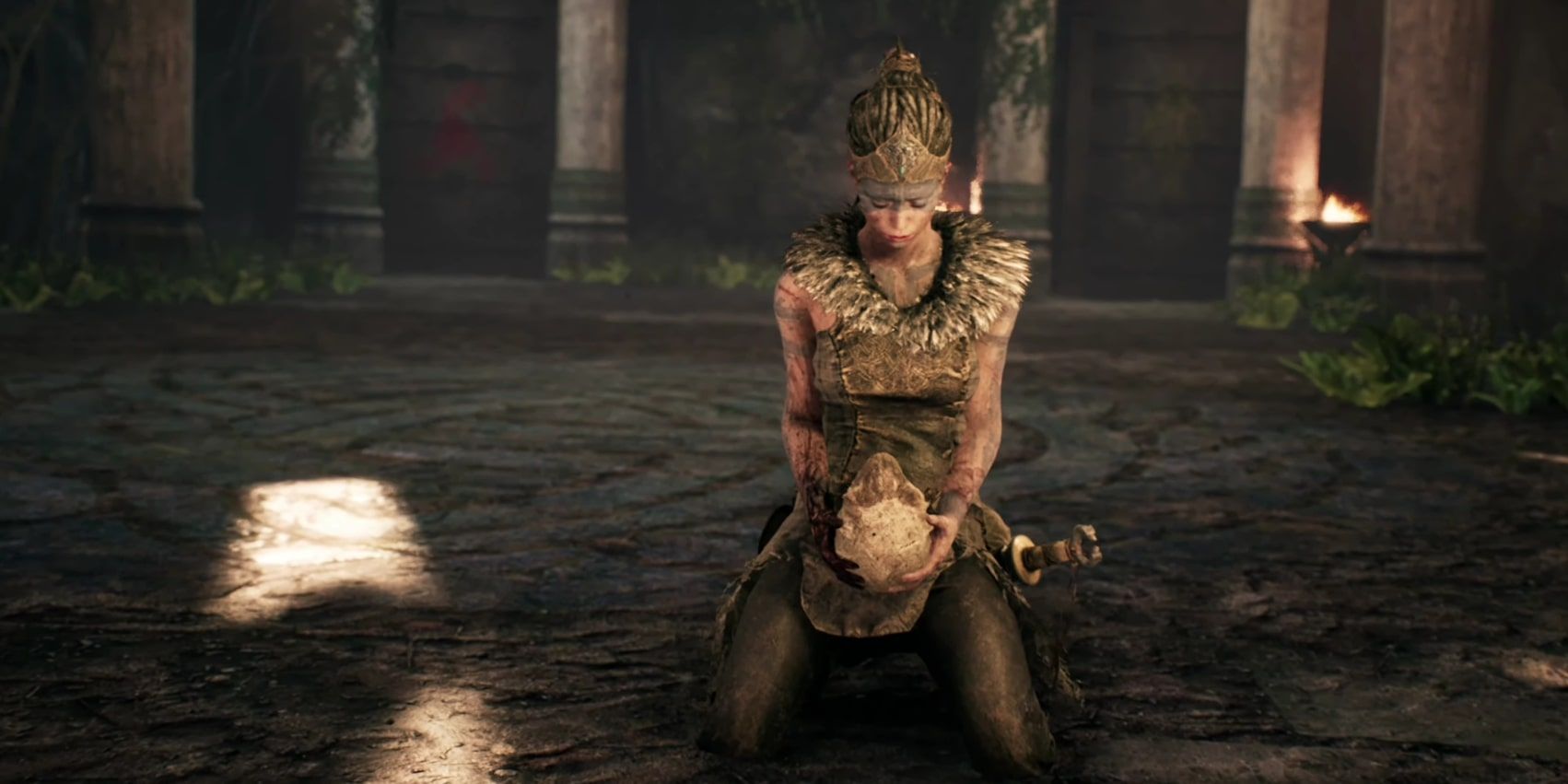 Screenshot von Senua, die auf einen Schädel herabblickt, den sie in Hellblade hält.