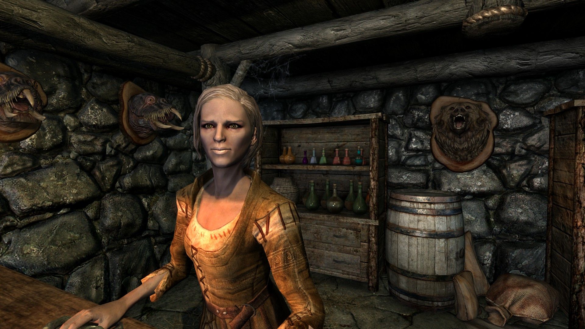 An old woman leans on the counter at her shop with a selection of potions on a shelf behind her.