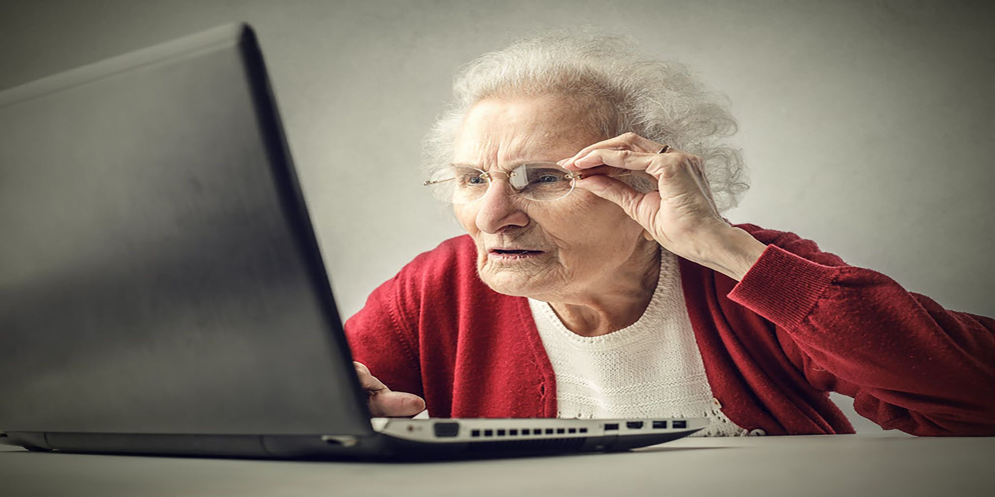 A distressed old woman stares at a laptop screen in confusion.