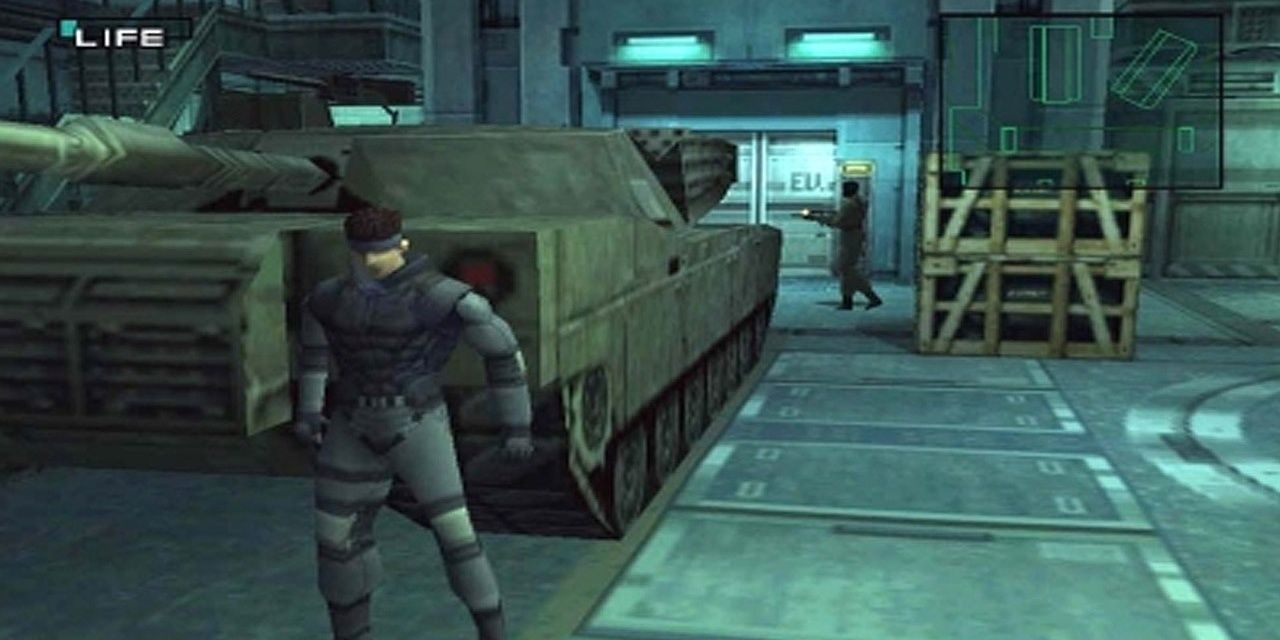 Snake hiding behind a tank inside a facility while an enemy soldier is patrolling.