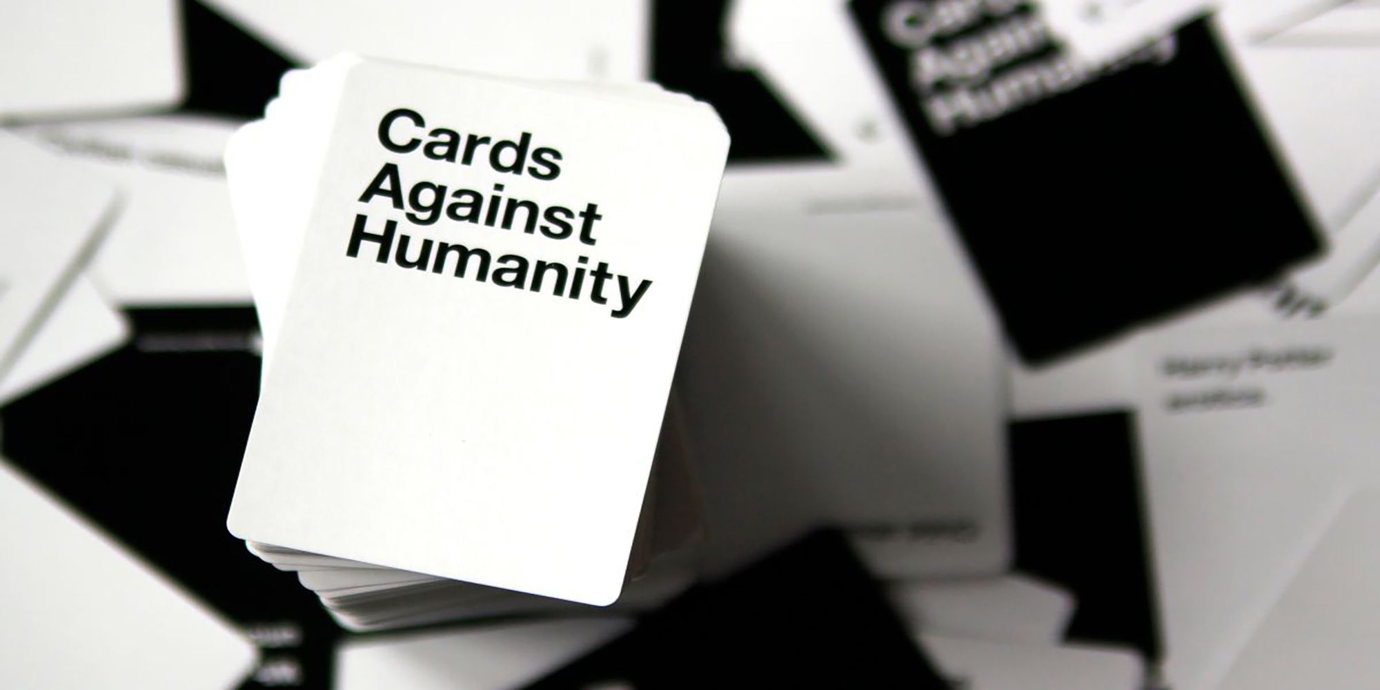 A Cards Against Humanity card deck, sits atop a table of black and white game cards.