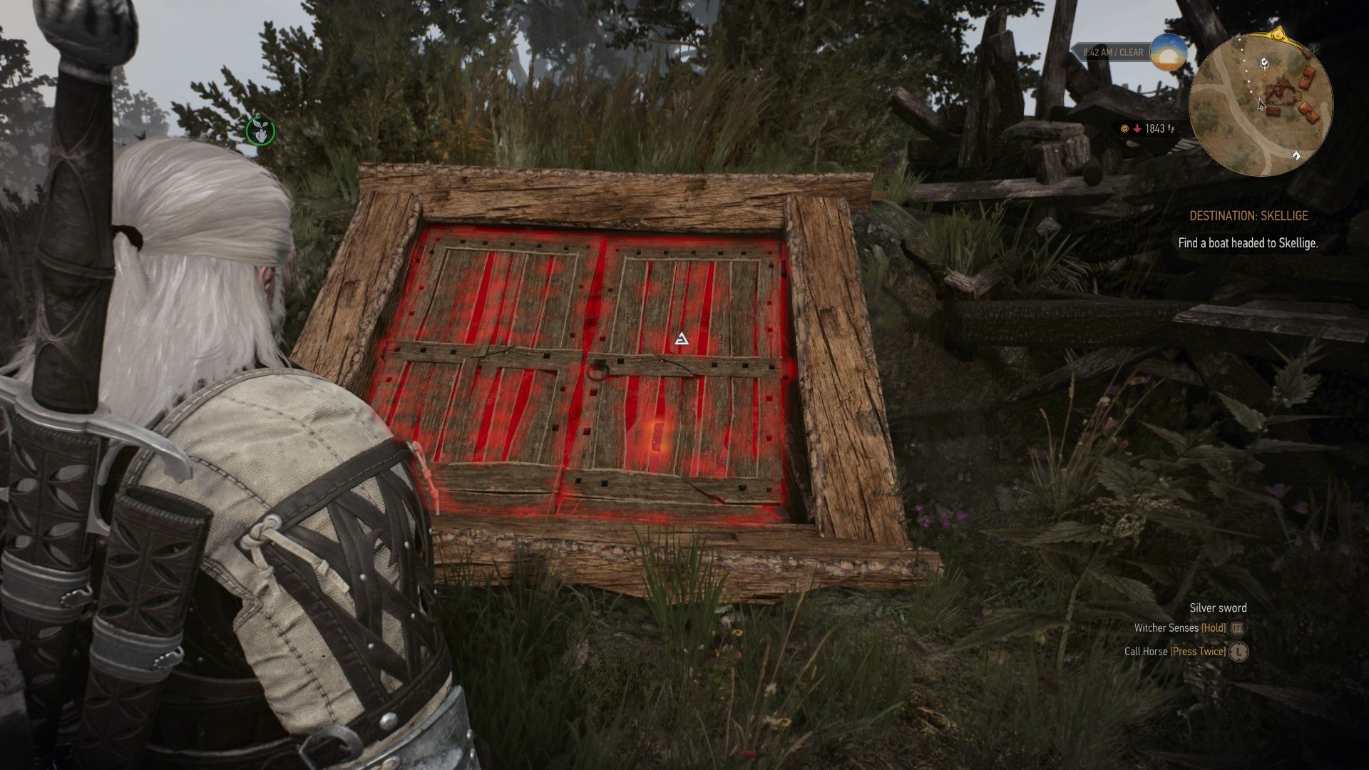 A screenshot of Geralt staring at a cellar entrance near a burned village with the wood glowing under his Witcher Senses.