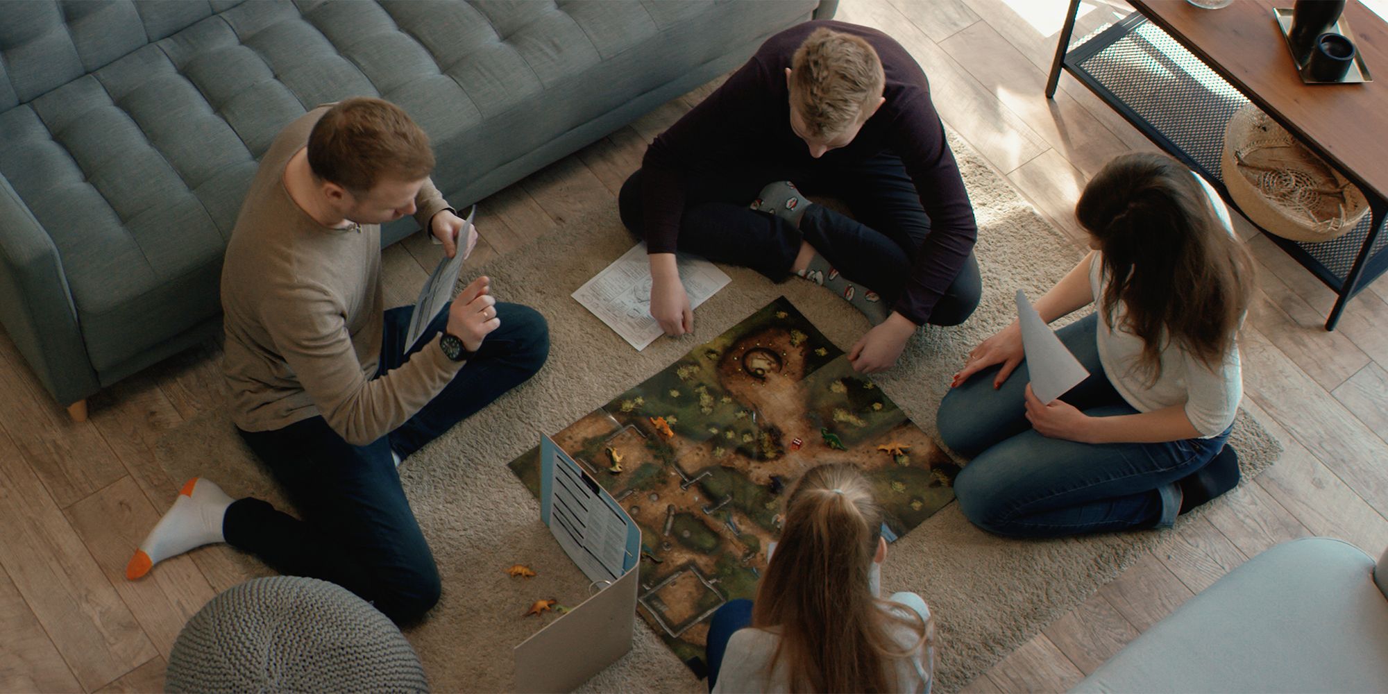 Four people on the floor in front of the sofa around a Dungeons & Dragons board