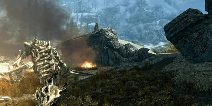 A skeleton of a dragon rests on the ground as the Dragonborn stands behind it, triumphant, on a rocky incline.