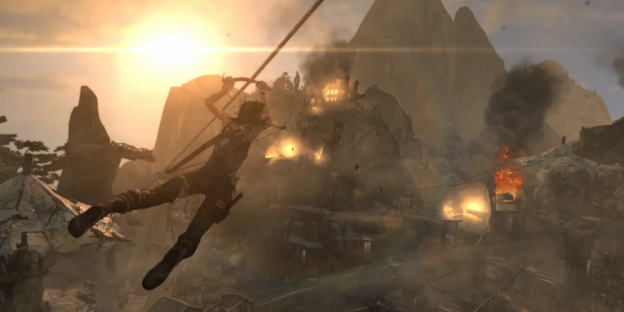 Lara Croft of Tomb Raider uses a small pickaxe to zipline across a rope towards a burning village.