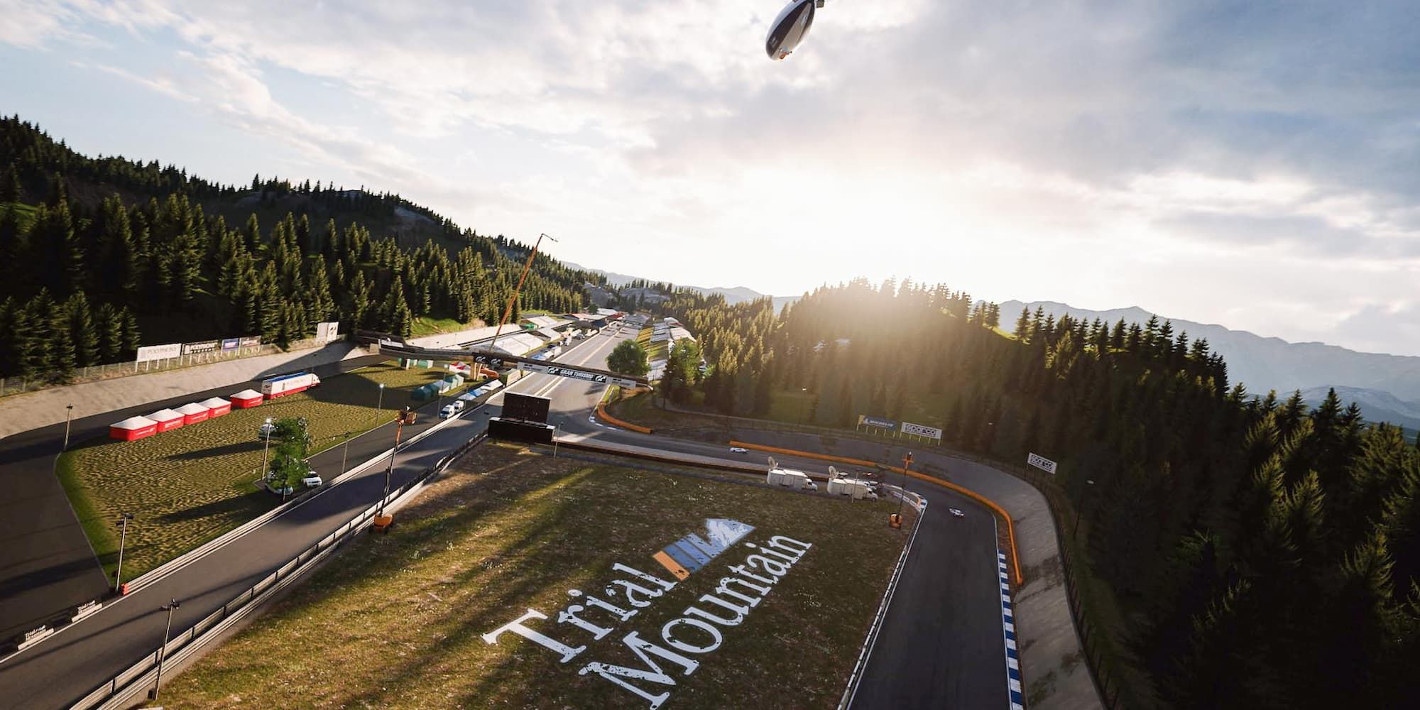 An overview shot of Trial Mountain in Grand Turismo 7 with a blimp above and a sunrise over the trees.